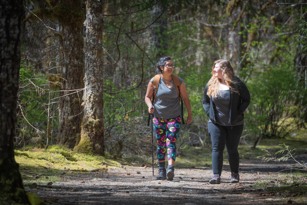 Two women hiking on a flat gravel path through a forest
